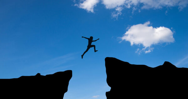 Man jump through the gap between hill.man jumping over cliff on sunset background,Business concept idea